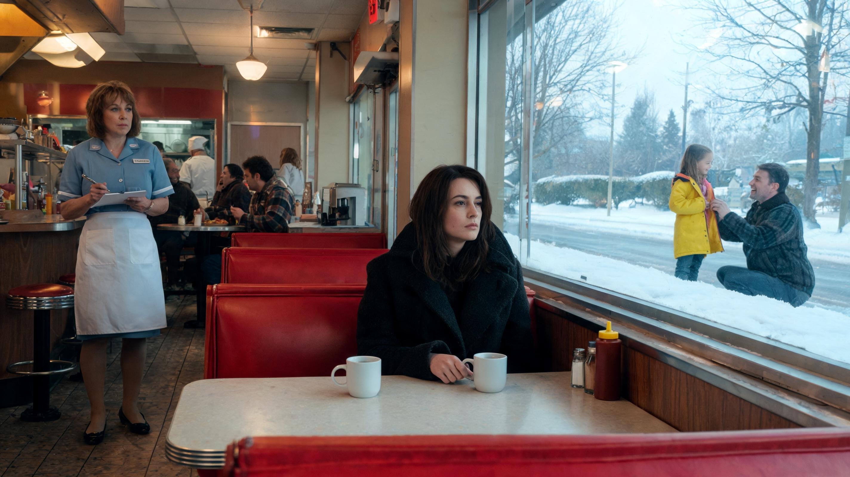 A young woman in a black coat sits alone in a classic American diner booth, two untouched coffee mugs on the table, staring out the winter window at a father laughing in the snow with his young daughter in a yellow coat — invisible grief while ordinary life continues