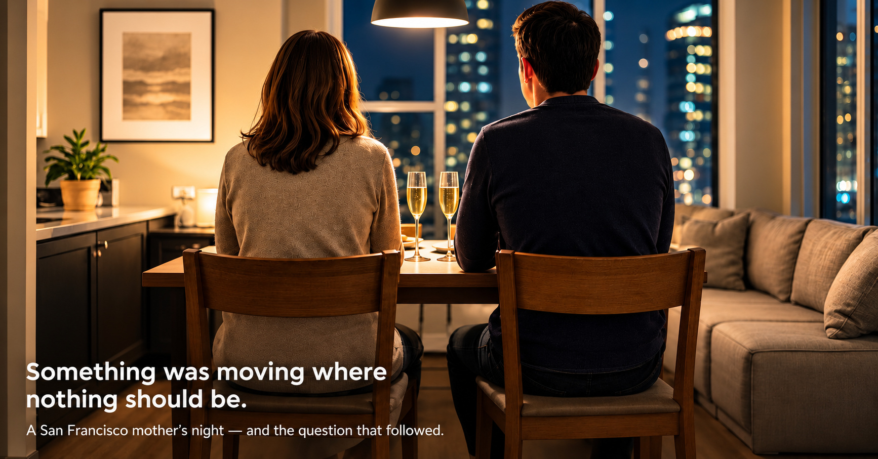 A couple seen from behind at a small dining table in a warmly lit apartment at night, champagne glasses between them, faces not visible